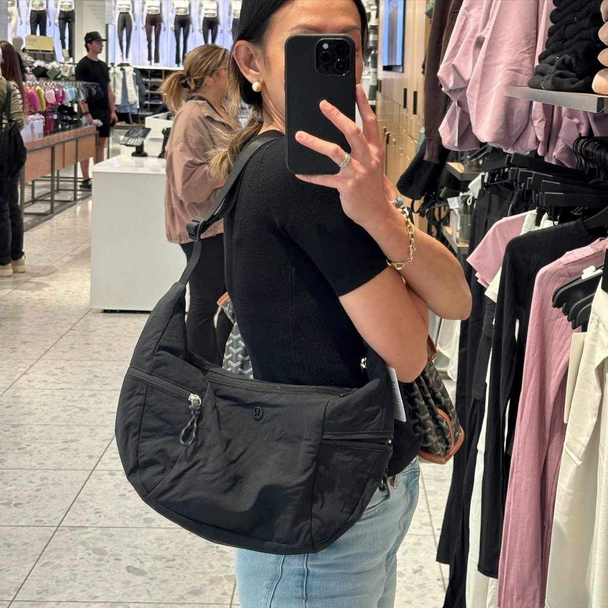 Person wearing a black lululemon slouchy sling bag while taking a mirror selfie.