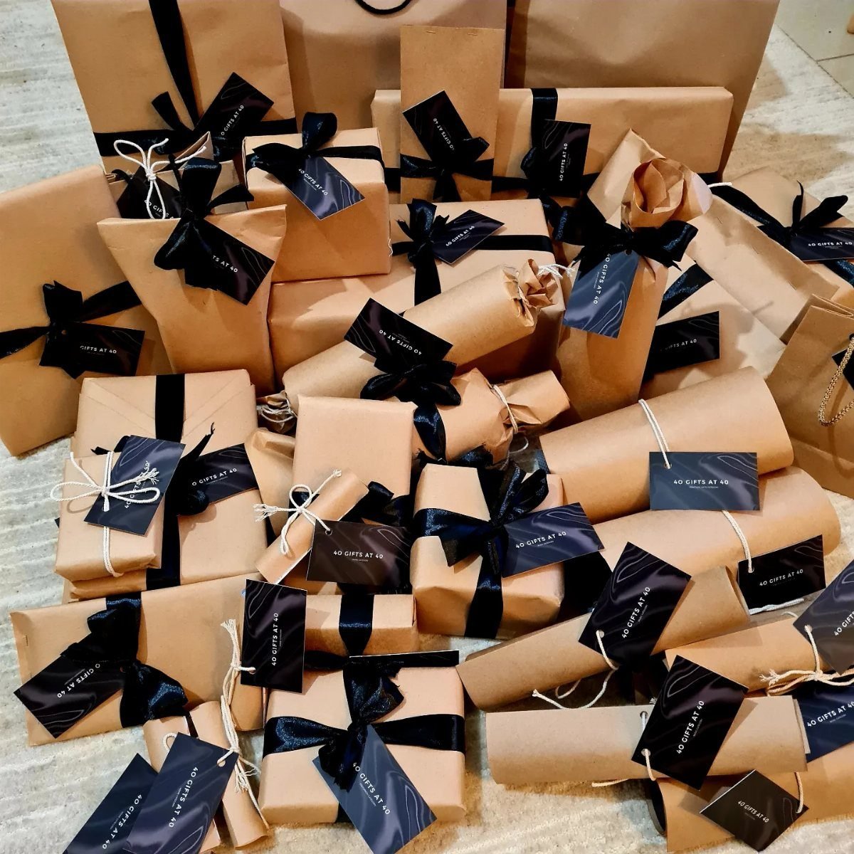 Brown paper wrapped gifts with black ribbons and tags piled on a floor.