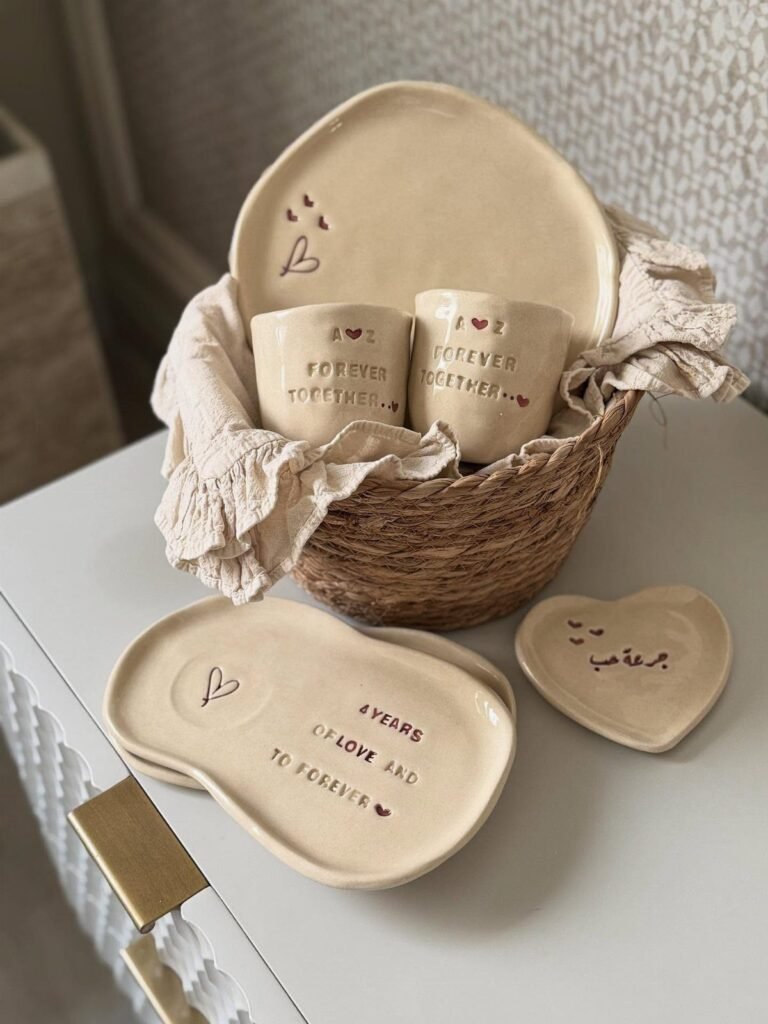 Cream ceramic dishes and cups with stamped text in a woven wicker basket.