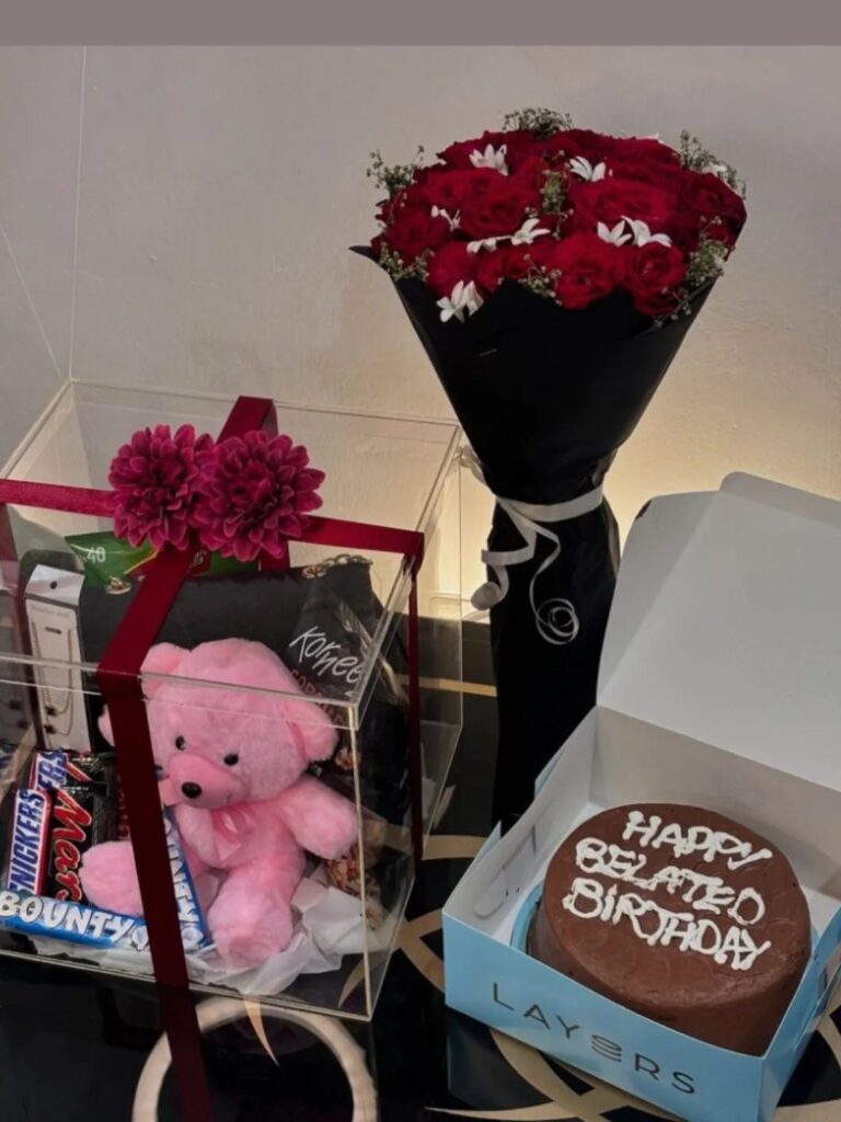 Chocolate birthday cake, red rose bouquet, and a pink teddy bear gift box.