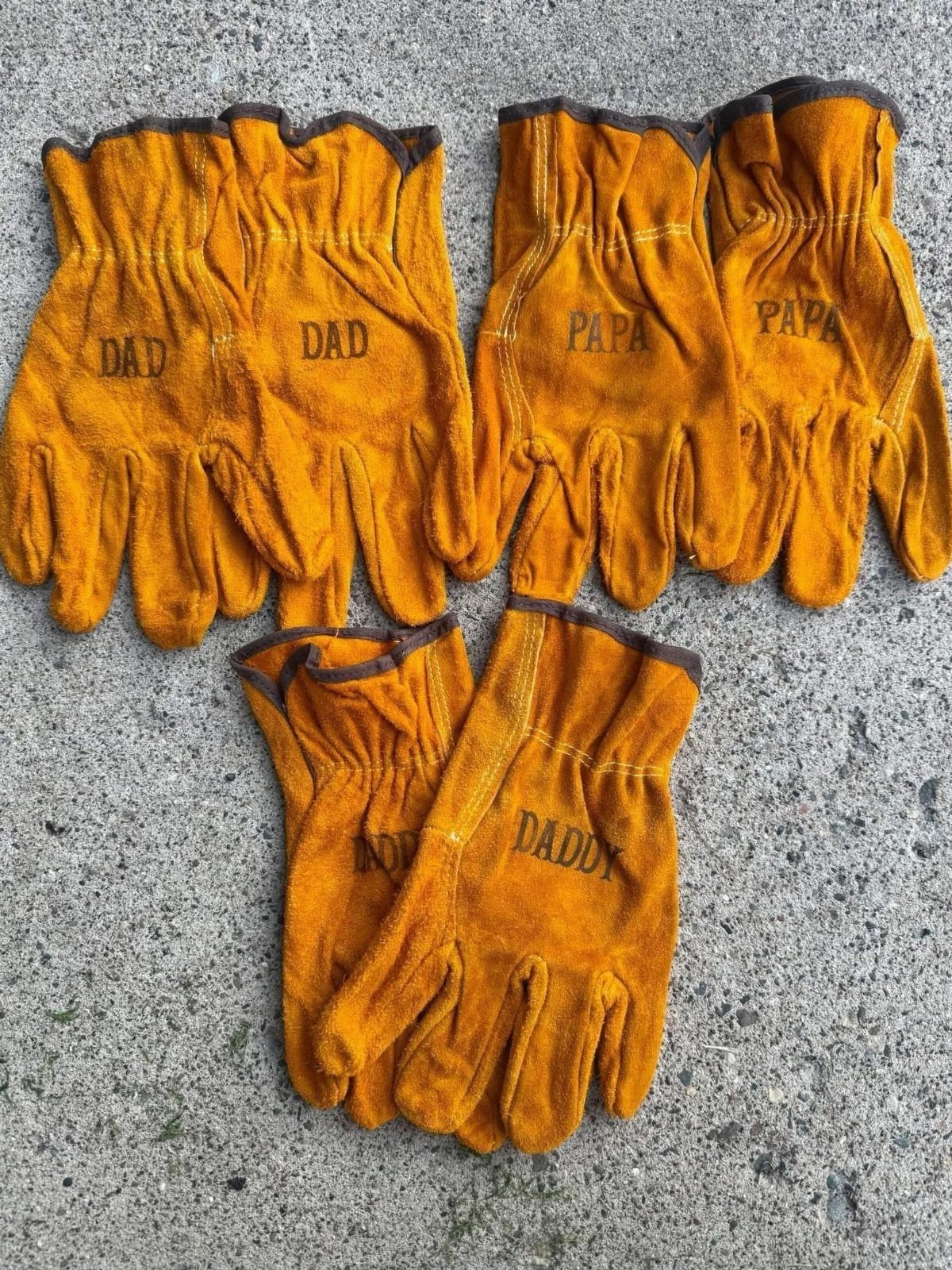 Tan leather work gloves with Dad, Papa, and Daddy printed on them.