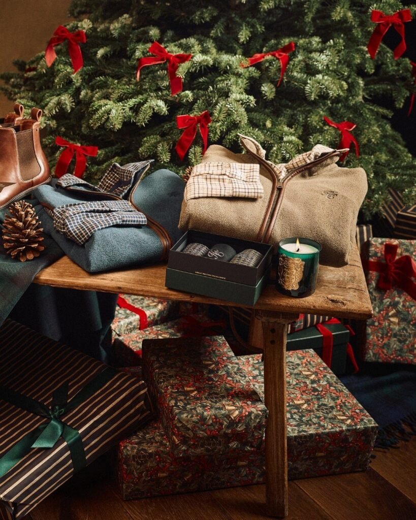 Folded beige sweater and blue plaid shirt on a table near a Christmas tree.