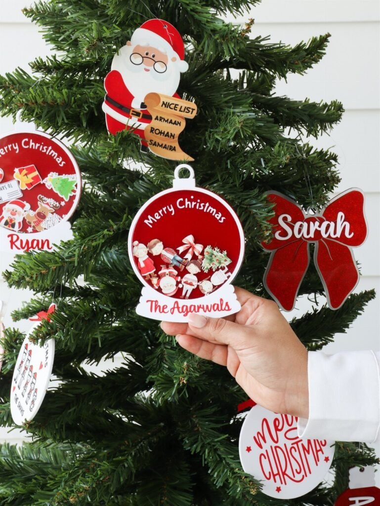 Hand holding a personalized circular Christmas ornament with family name on a tree