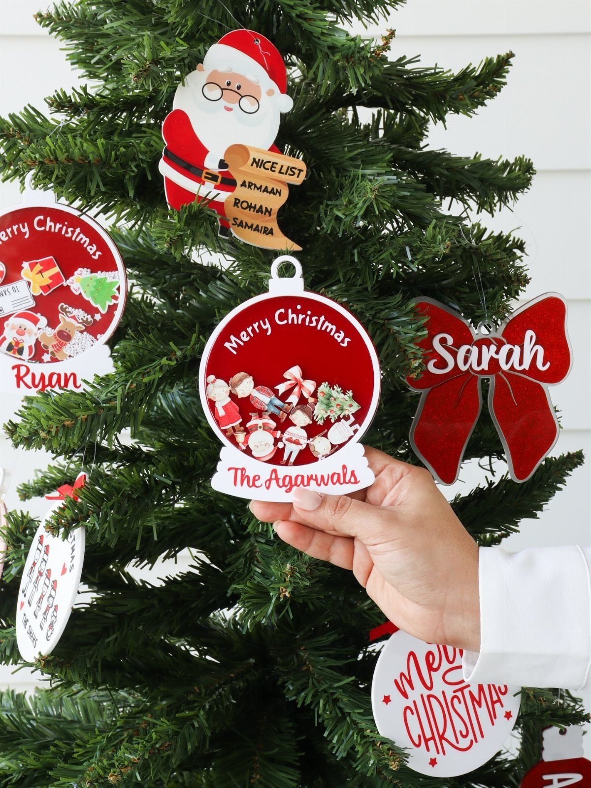Hand holding a personalized circular Christmas ornament with family name on a tree