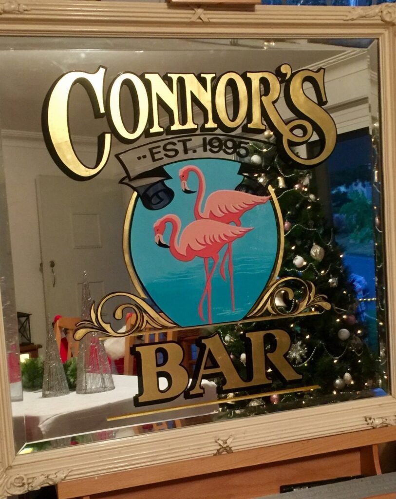 Personalized mirrored bar sign with gold lettering and pink flamingos near a Christmas tree