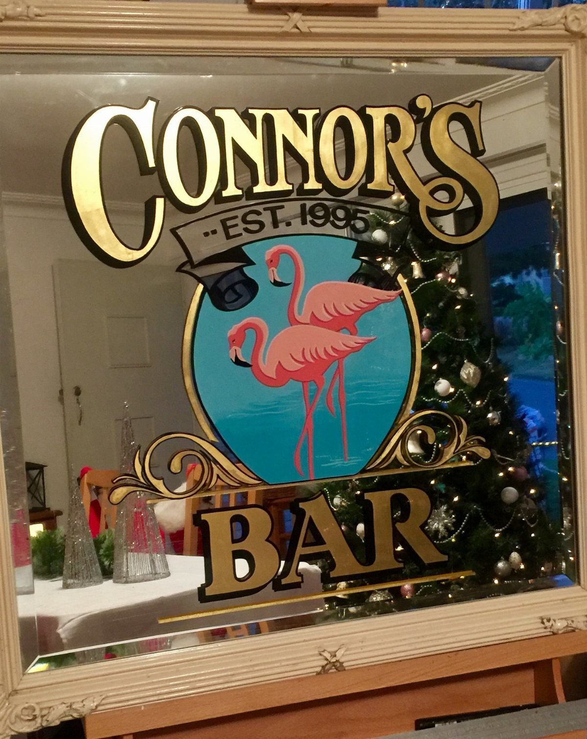 Personalized mirrored bar sign with gold lettering and pink flamingos near a Christmas tree