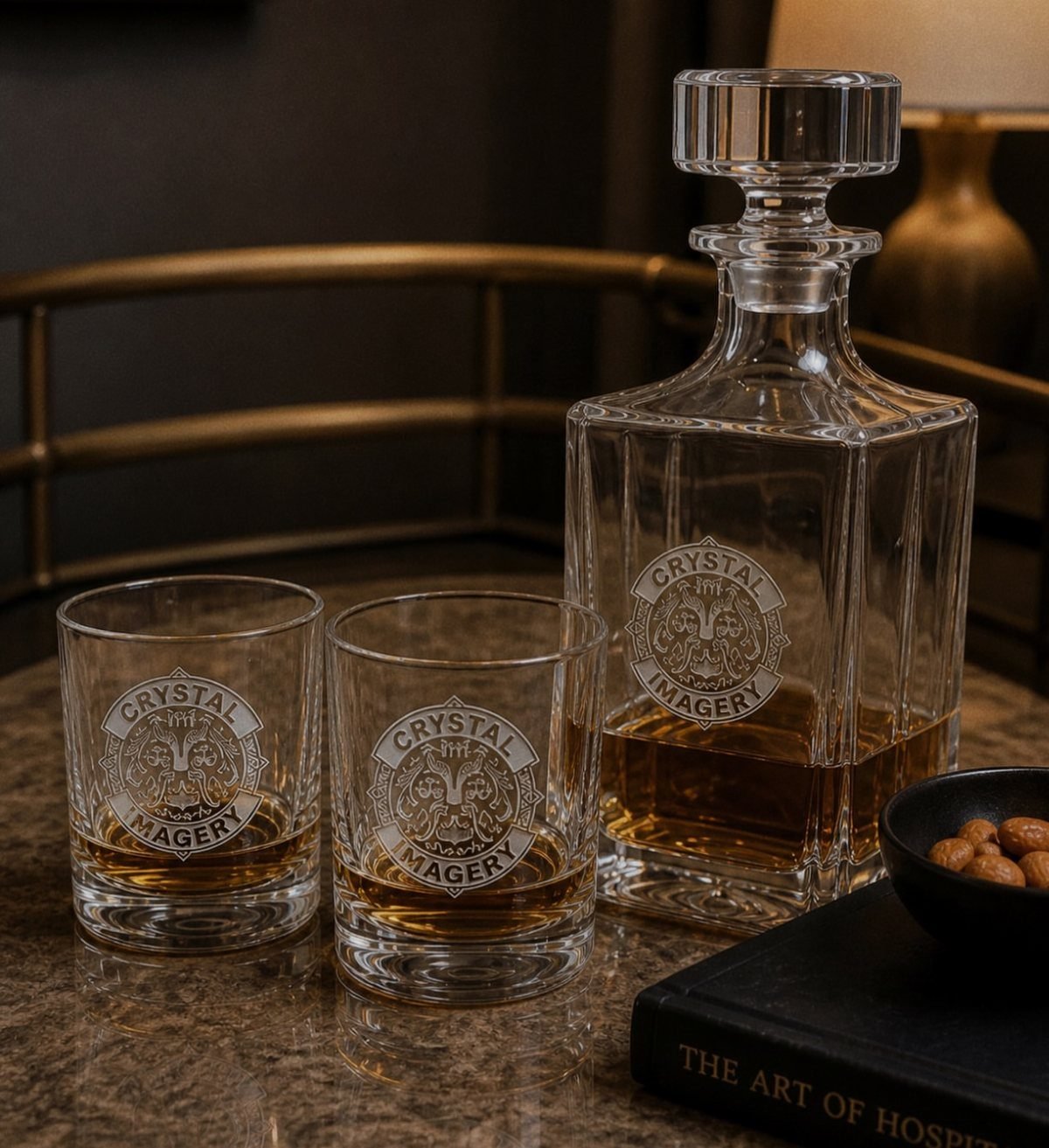 Glass decanter and two tumblers with etched logos filled with amber liquor.