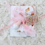 Wrapped gift with pink ribbon and wooden name tag on white shaggy rug