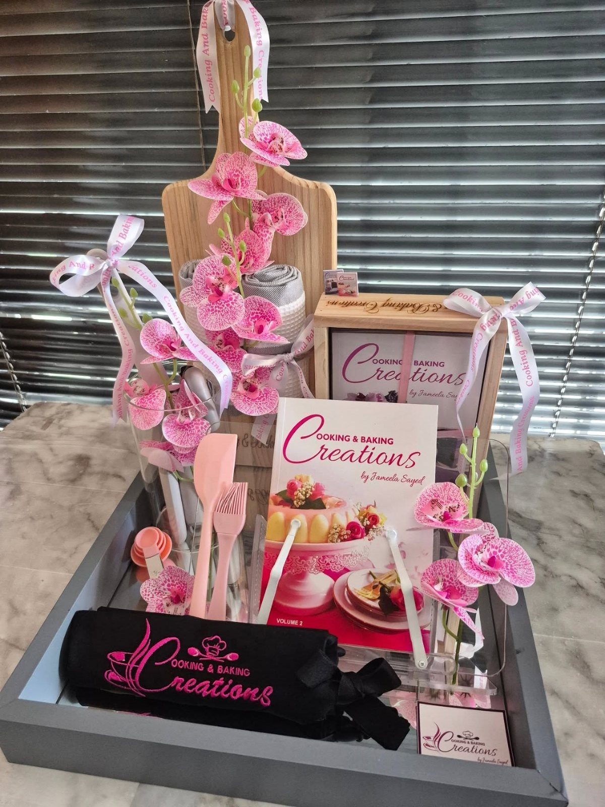 Cooking and baking cookbook with pink utensils and orchids in a gift tray.