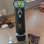 Black FIZZICS beer dispenser with Guinness branding and accessories on a wooden floor.
