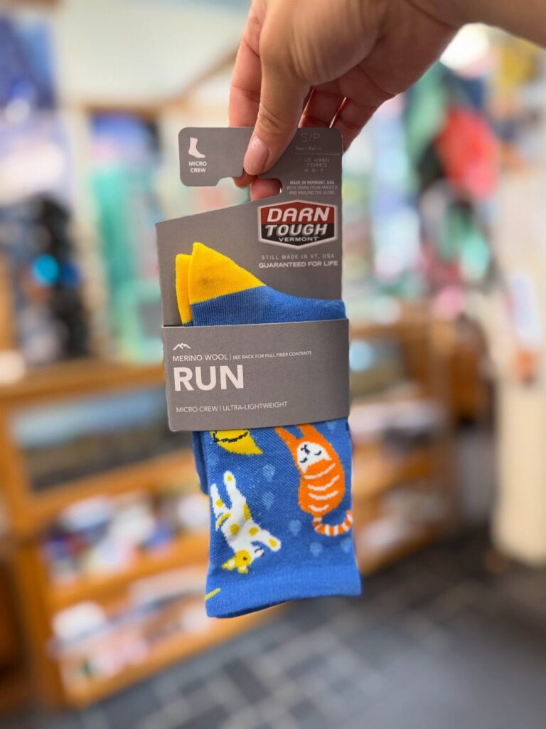 Blue running socks with cat patterns in Darn Tough brand packaging held by hand.