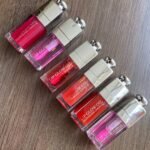 Six Dior Lip Glow Oil tubes in pink and red shades on wood.