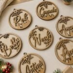 Wooden circular Christmas ornaments with personalized names and snowflake designs on a table.