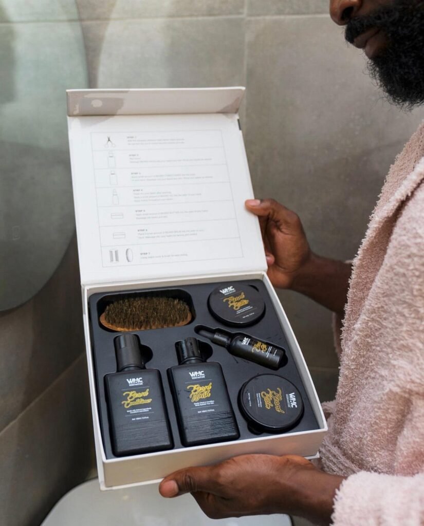 Man holding an open white box containing a complete beard grooming kit.
