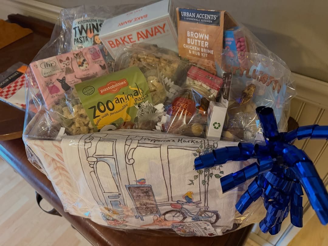 Gourmet gift basket wrapped in cellophane with various food items and blue bow.
