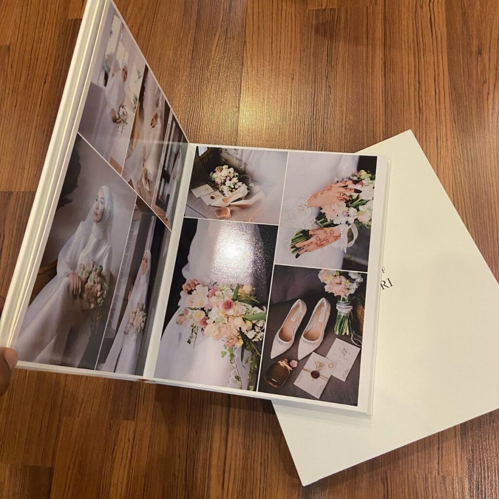 Open white photo album with wedding pictures resting on a wooden floor.