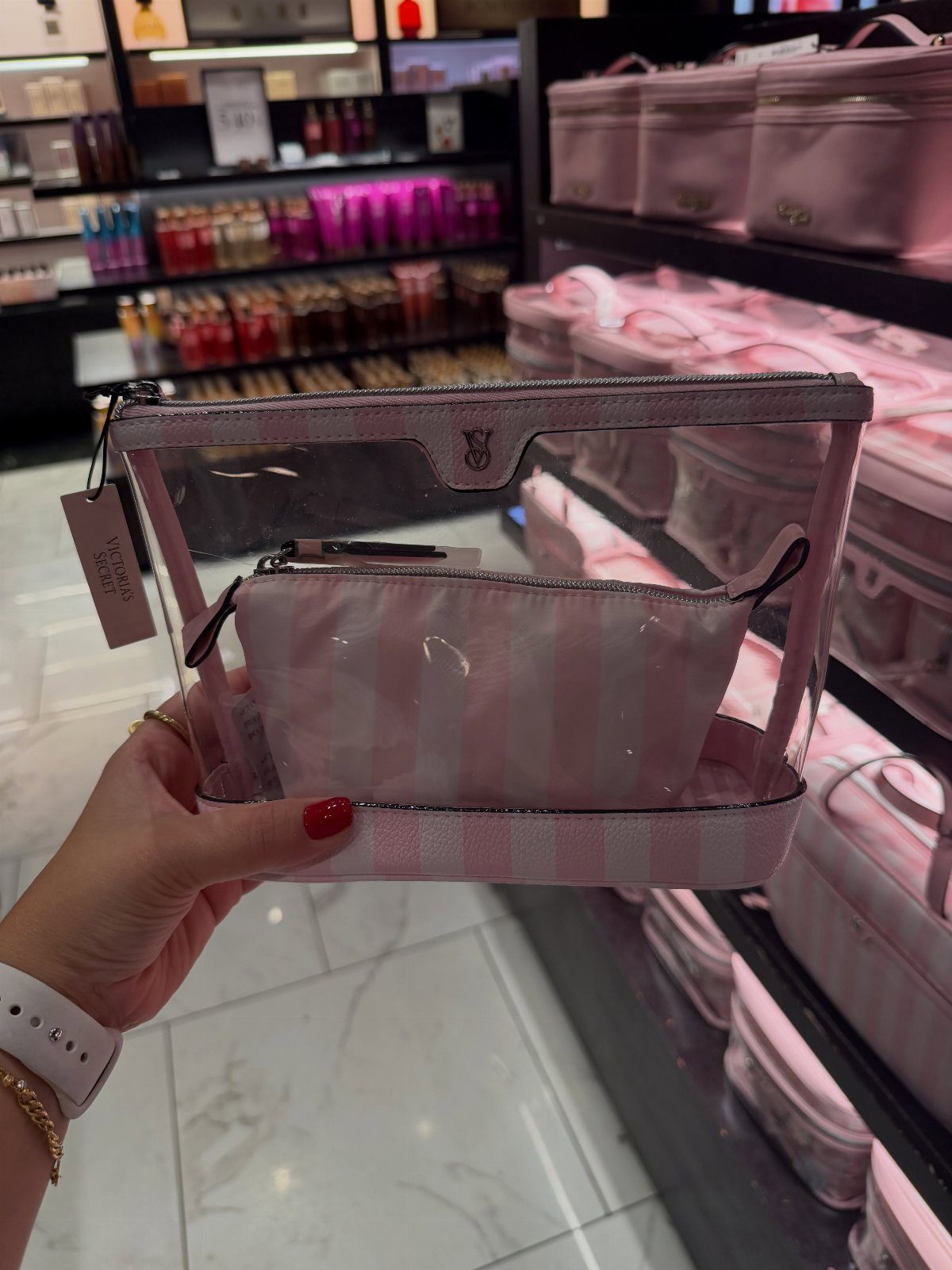 Clear and pink striped travel makeup bag held in a beauty store setting.