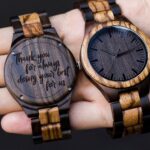Two wooden wristwatches, one showing the face and one showing an engraved back.
