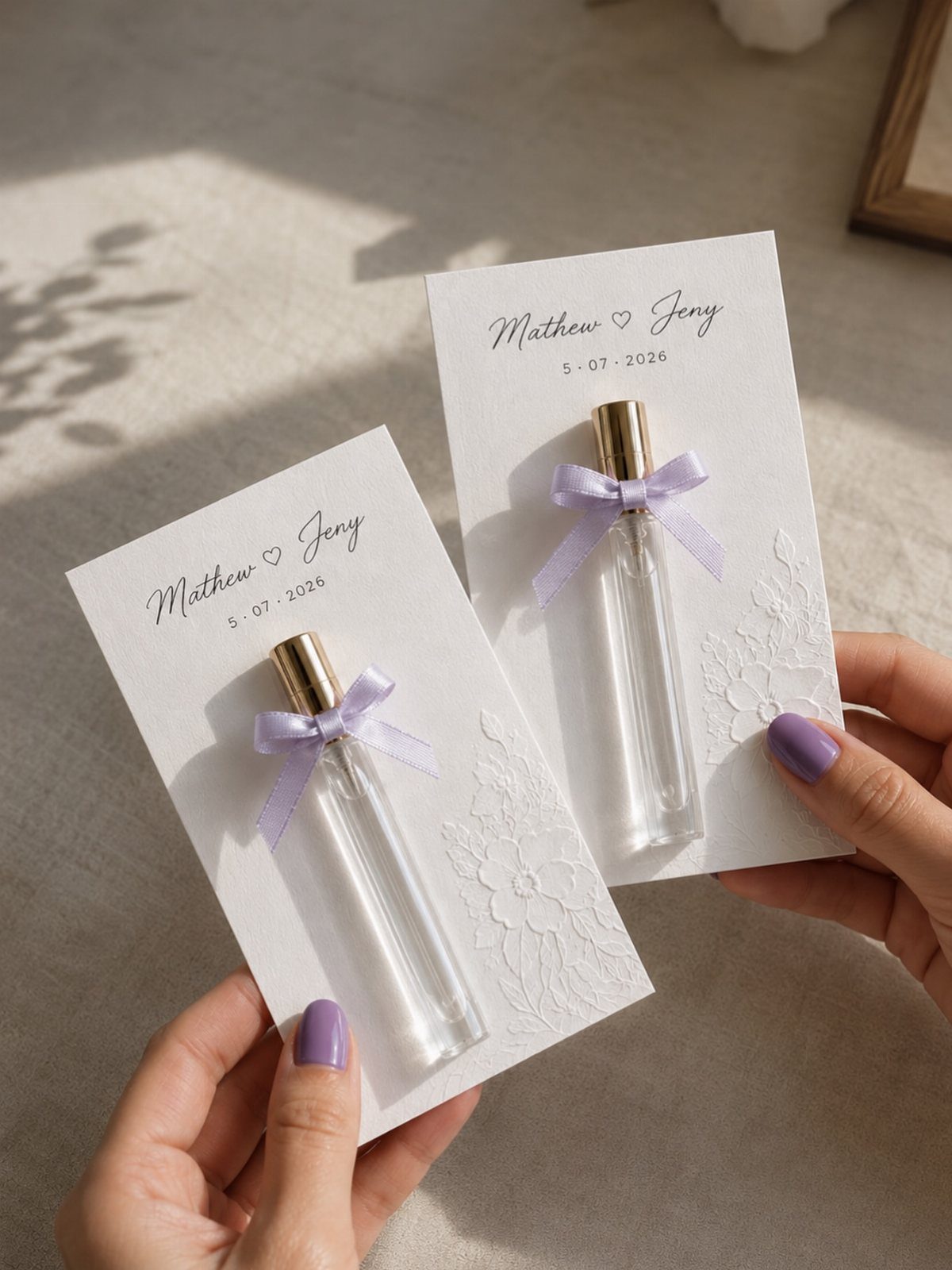 Small perfume bottles with purple bows on personalized wedding gift cards held by hands