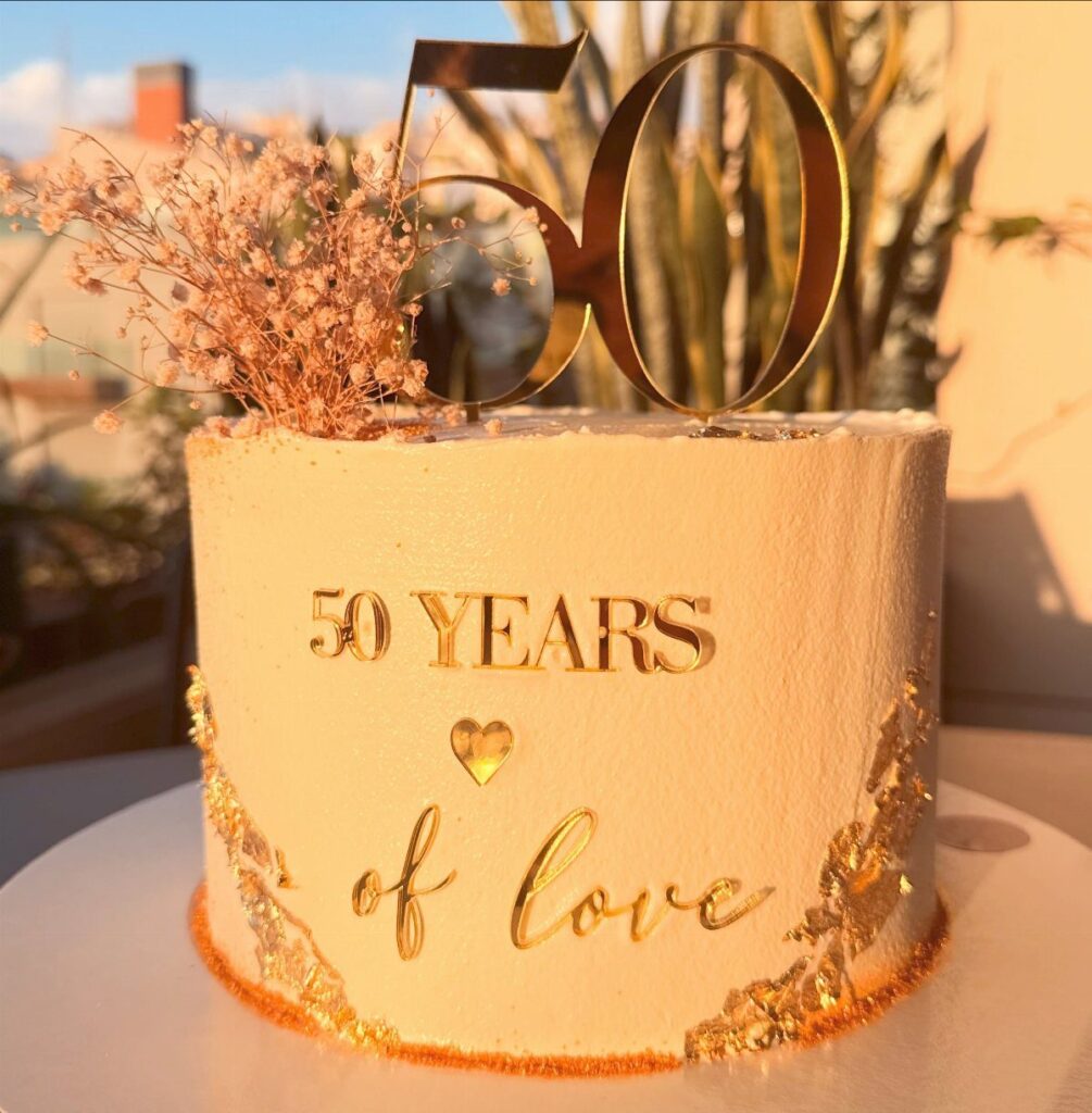 White anniversary cake with gold 50 topper and gold lettering saying 50 years of love